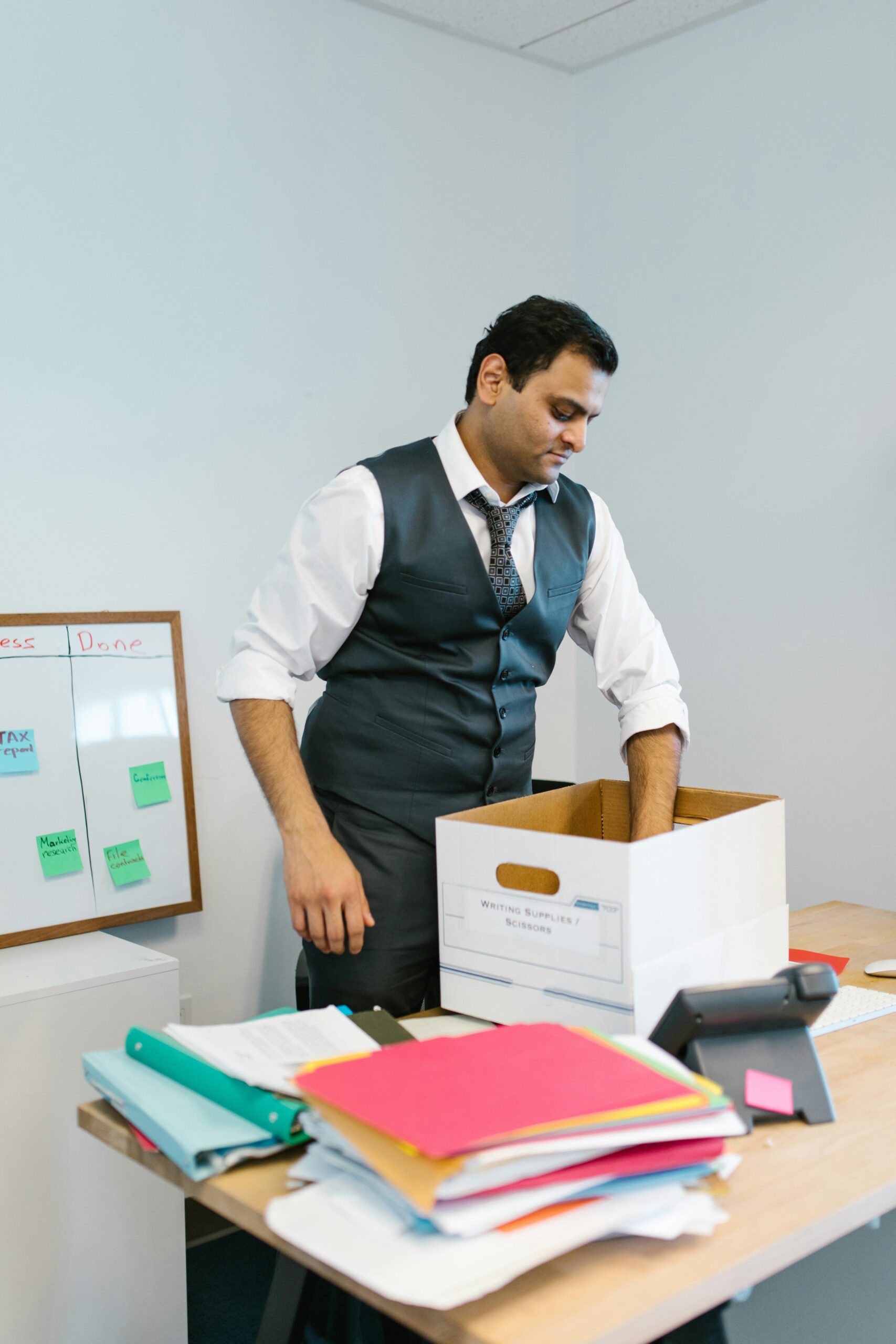 Professional man packing belongings into a box at an office desk, preparing to leave the workplace.