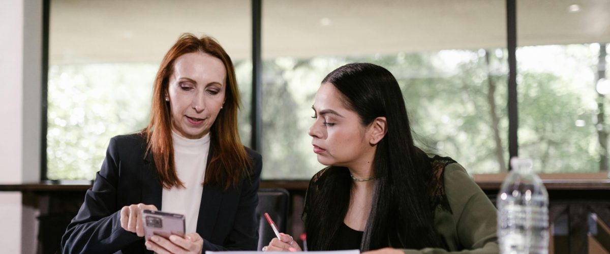 Two professional women collaborating with documents and smartphone in a meeting room.